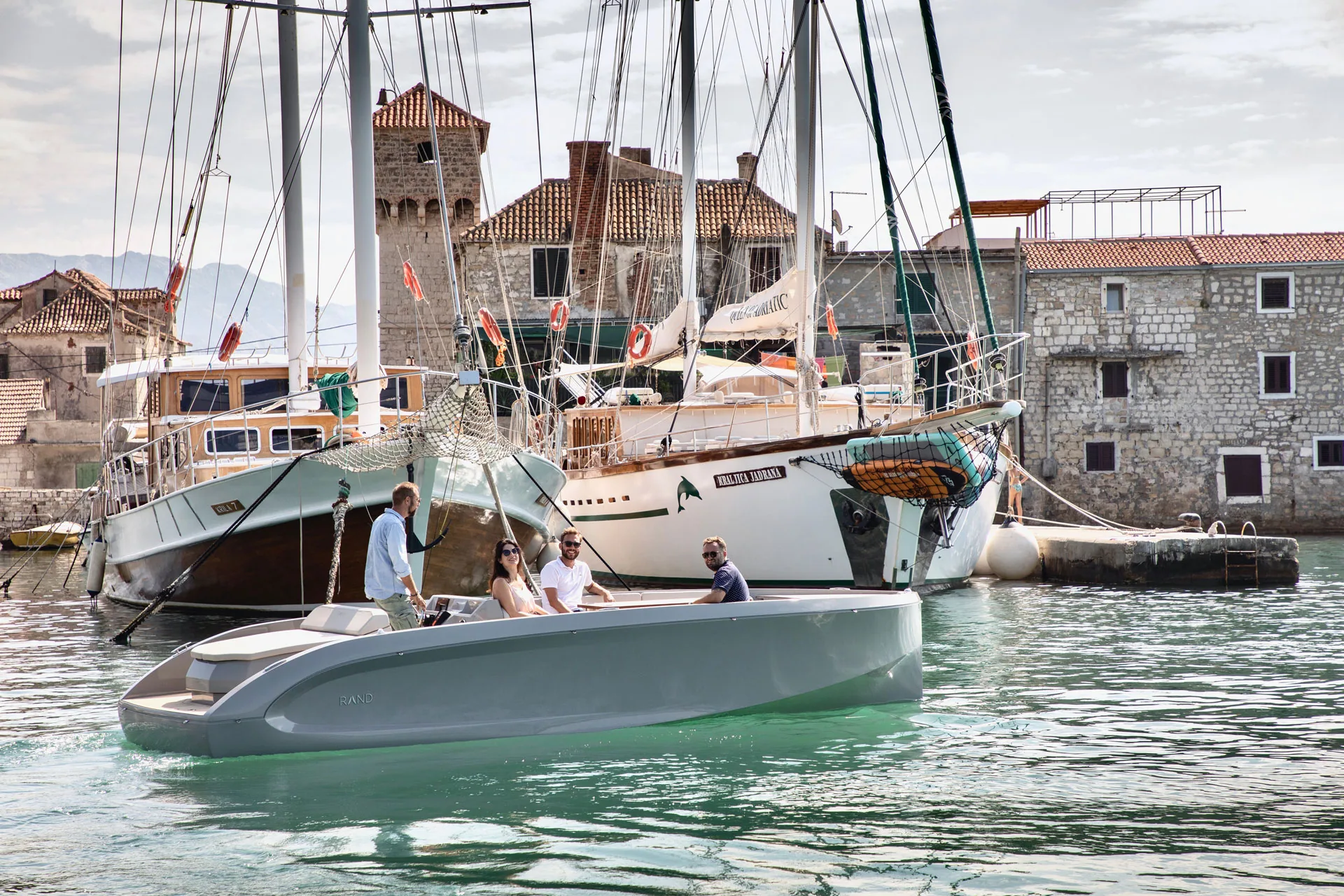 A RAND leaving a stone harbour among classic sailing ships